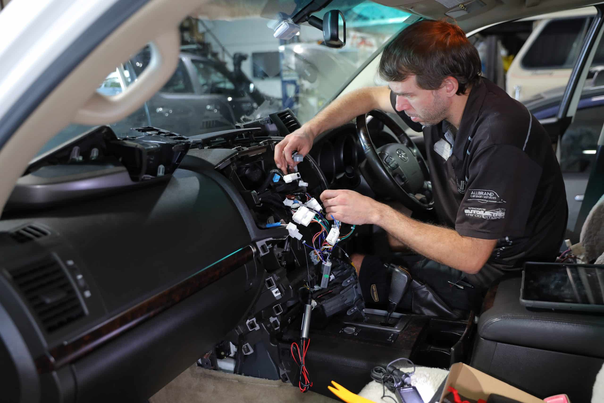 Technician troubleshooting car electrical issues inside a workshop